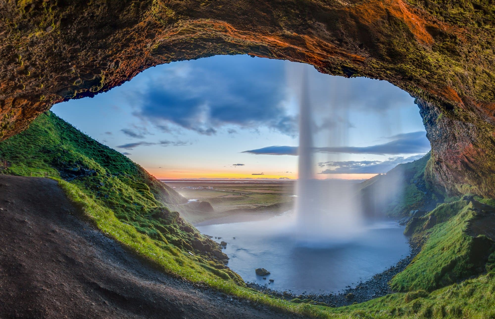 Seljalandsfoss vue de derrière le rideau d’eau, la vallée verte au loin