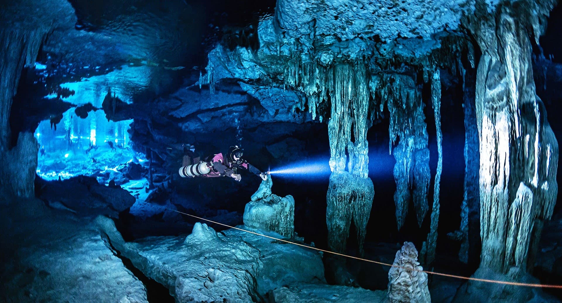 Plongeur à la lampe entre les stalactites d’un cénote
